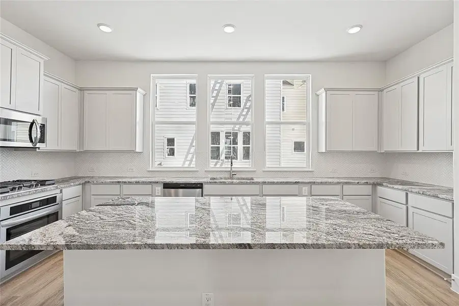 The kitchen features an expansive island with a granite countertop, stainless steel appliances, and white cabinetry