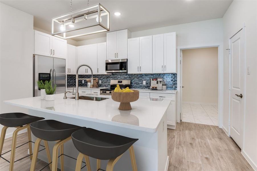 Kitchen featuring stainless steel appliances, white cabinets, tasteful backsplash, a center island with sink, and light stone counters