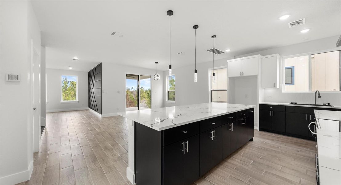 Kitchen with dark cabinetry, a kitchen island, wood tiled floors, light stone countertops, and recessed lighting