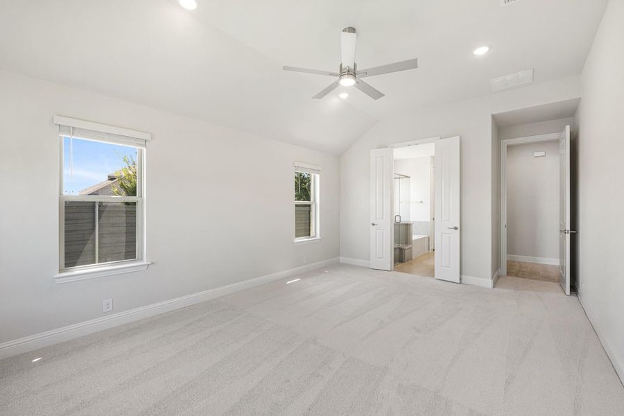 Spacious master bedroom with vaulted ceiling, ceiling fan, carpet, and doors leading to ensuite bathroom and walk-in closet