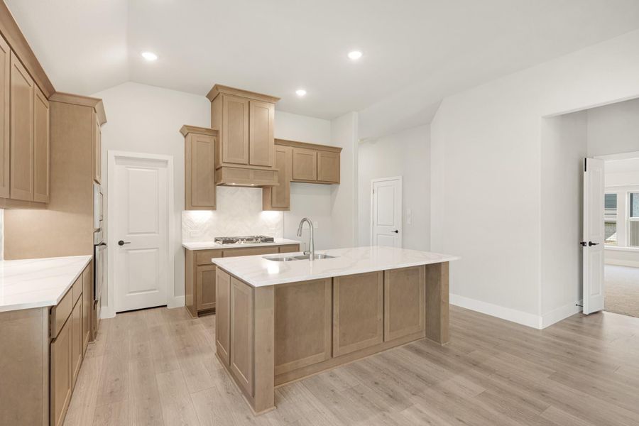 Kitchen with large center island, sink, light wood cabinets, white countertops, and light hardwood floors Kitchen with large center island, sink, light wood cabinets, white countertops, and light hardwood floors