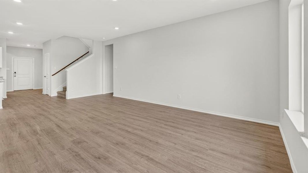 Spacious open-concept living area featuring wood-finish flooring, recessed lighting, neutral wall tones, and a staircase with dark wood-finish handrails