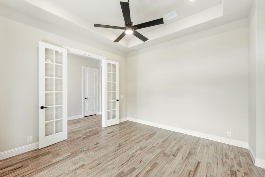 Empty room with hardwood floors, tray ceiling, ceiling fan, and white French doors Empty room with hardwood floors, tray ceiling, ceiling fan, and white French doors