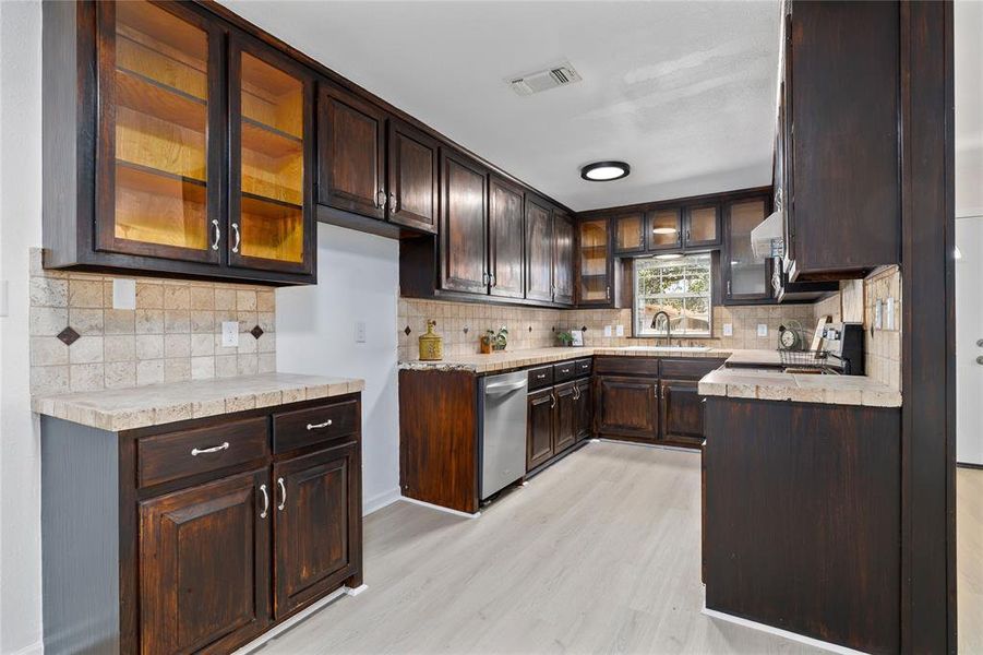 Kitchen featuring glass insert cabinets, dark brown cabinetry, light countertops, and light wood-type flooring