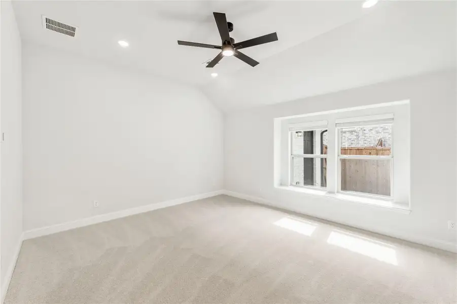 Empty bedroom with vaulted ceiling, ceiling fan, carpet flooring, and a large window