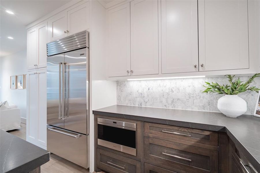 Kitchen with white cabinetry, dark brown cabinetry, stainless steel appliances, and decorative backsplash