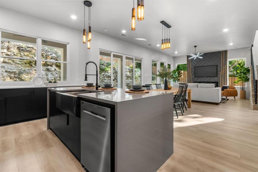 Kitchen featuring modern cabinets, dark cabinetry, hanging light fixtures, a center island with sink, and healthy amount of natural light