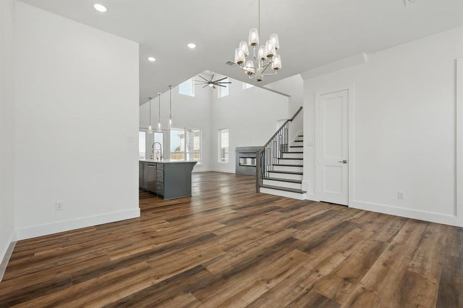 Unfurnished living room with dark wood-style floors, stairs, a sink, baseboards, and ceiling fan with notable chandelier