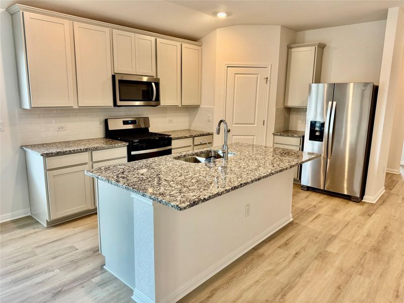 Kitchen featuring appliances with stainless steel finishes, light stone countertops, decorative backsplash, light wood-style floors, and an island with sink Kitchen featuring appliances with stainless steel finishes, light stone countertops, decorative backsplash, light wood-style floors, and an island with sink