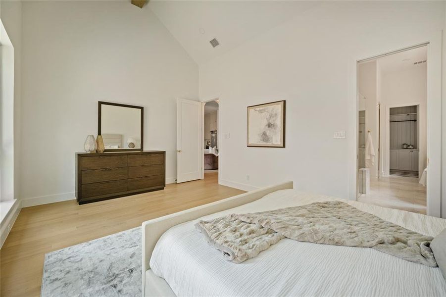 Bedroom with light wood finished floors, high vaulted ceiling, and arched walkways