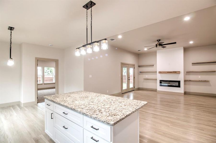 Kitchen with a kitchen island, open floor plan, hanging light fixtures, light wood-style floors, and light stone counters