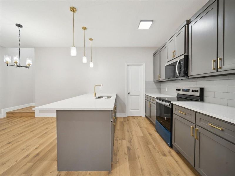 Kitchen with appliances with stainless steel finishes, backsplash, gray cabinetry, sink, and an island with sink