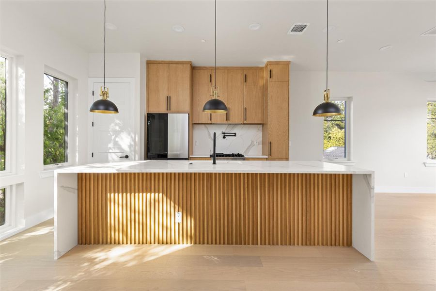 Warm wood tones complement a waterfall island under recessed lights in this open kitchen.