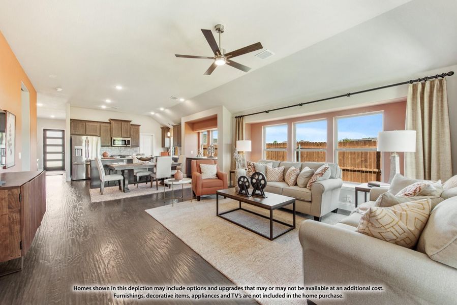 Open-concept living room with vaulted ceiling, ceiling fan, hardwood floors, and kitchen visible in background Open-concept living room with vaulted ceiling, ceiling fan, hardwood floors, and kitchen visible in background