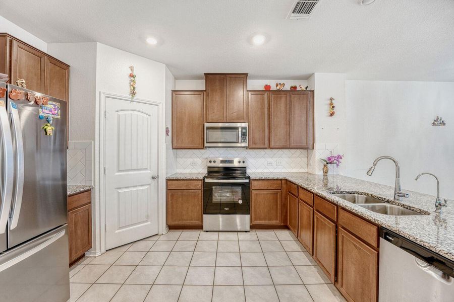 Kitchen featuring brown cabinets, appliances with stainless steel finishes, light stone countertops, and tasteful backsplash