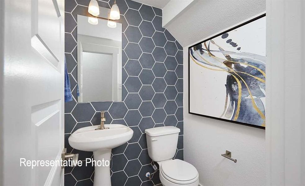 Powder room featuring a pedestal sink, toilet, and hexagonal wall tiling