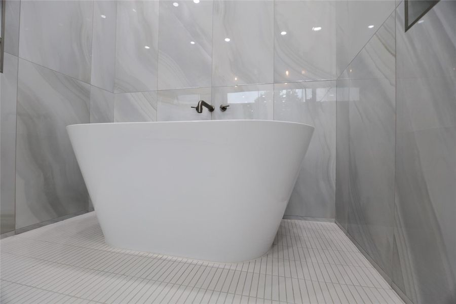 A stunning Woodbridge soaking tub is beautifully surrounded by large-profile tiles, creating a serene, spa-like ambiance that complements the rest of the en suite. A stunning Woodbridge soaking tub is beautifully surrounded by large-profile tiles, creating a serene, spa-like ambiance that complements the rest of the en suite.
