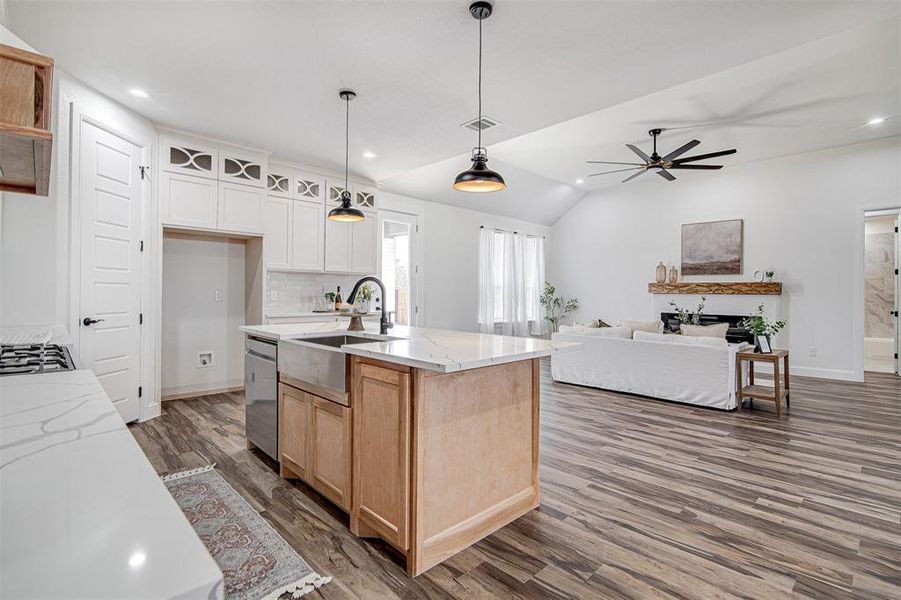 Kitchen featuring white cabinets, vaulted ceiling, light stone counters, and an island with a farm sink