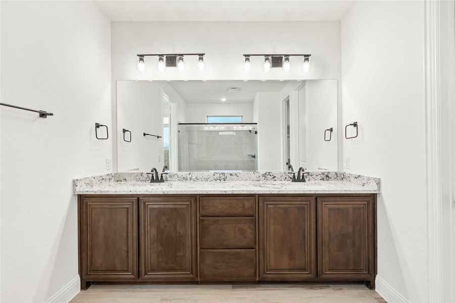 Bathroom double vanity with dark wood cabinets, granite countertop, two sinks, and large mirror with overhead lighting Bathroom double vanity with dark wood cabinets, granite countertop, two sinks, and large mirror with overhead lighting