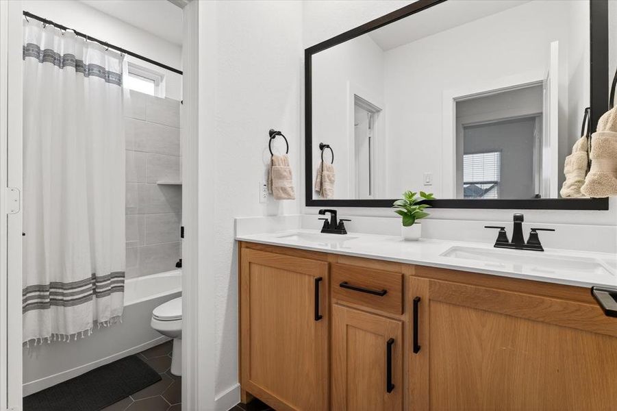 Bathroom featuring double vanity, shower / bathtub combination with curtain, and dark tile patterned flooring Bathroom featuring double vanity, shower / bathtub combination with curtain, and dark tile patterned flooring