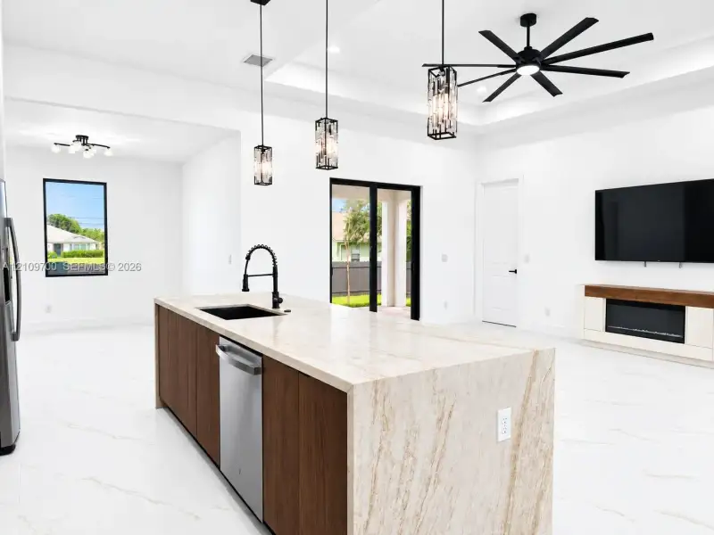 Large kitchen island with a stone-finish countertop, dual-tone cabinetry, recessed ceiling with a multi-blade fan, custom pendant lighting, and an integrated electric fireplace