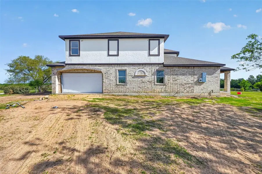 Side exterior view of Property 1 unfinished residence featuring attached garage, and surrounding open land.