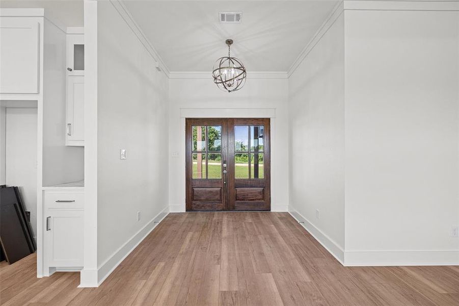 Double entry doors with divided lites, wood-finish flooring, recessed lighting, crown molding, and built-in cabinetry
