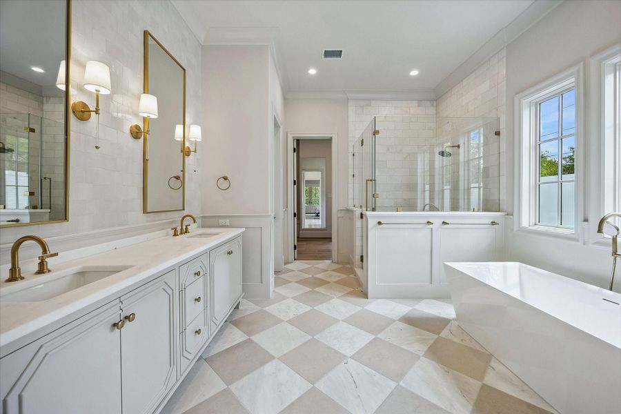 The luxurious primary bath reveals a beautifully designed dual vanity with custom designed cabinetry, marble countertops, and designer sconces flanking the beautiful, framed mirrors. The marble and limestone 18x18 checkerboard flooring continues throughout, complementing the sophisticated palette, while thoughtful details and high-end finishes create a cohesive and luxurious primary suite bath.