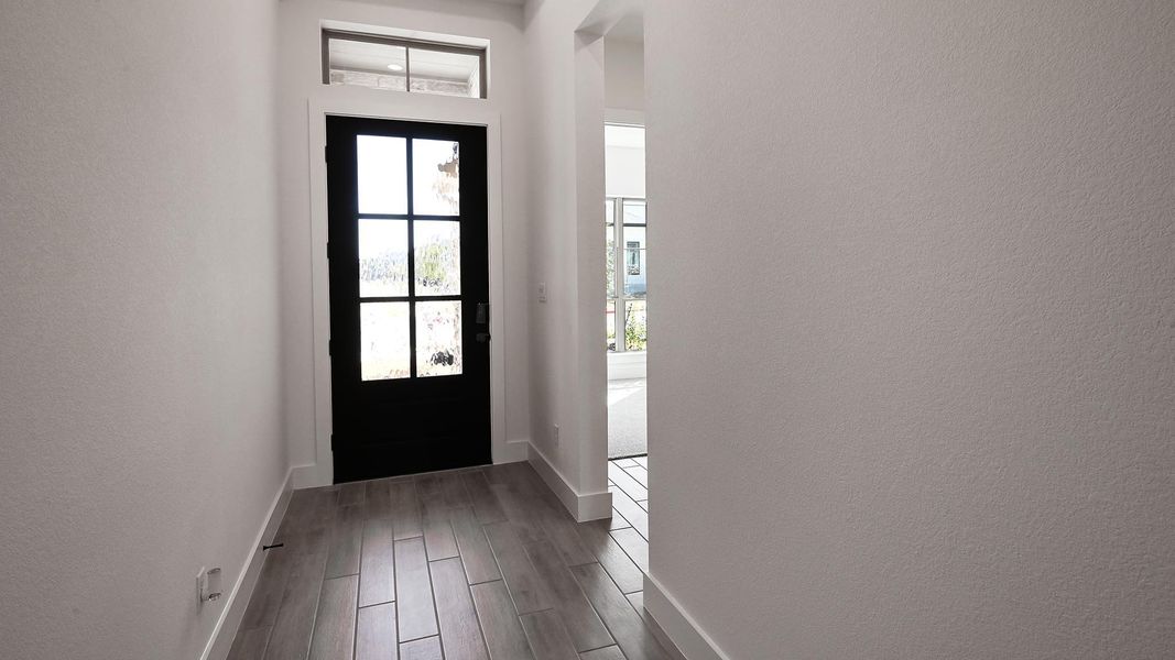 Doorway featuring a textured wall, baseboards, and wood finished floors