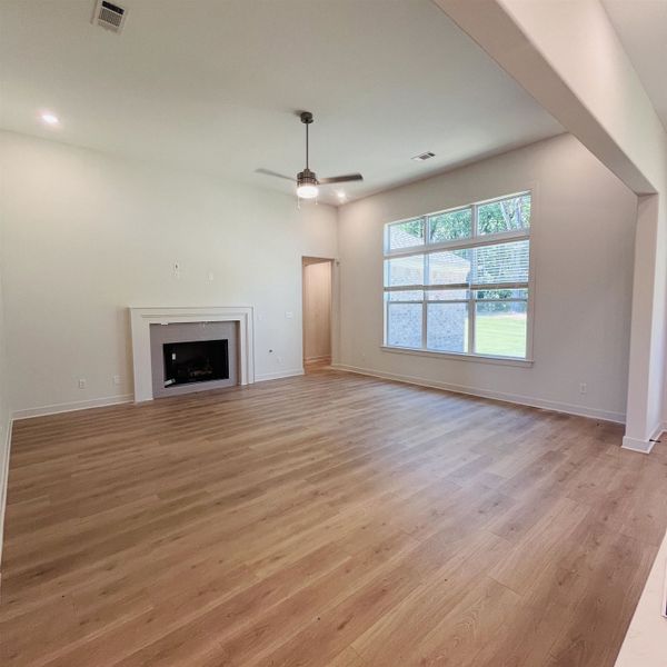 Spacious interior featuring wood-finish flooring, a fireplace with a white mantel, an overhead ceiling fan, and large windows with blinds