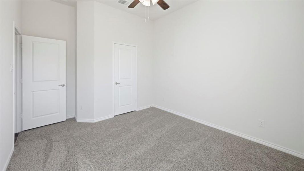Room featuring light gray carpeting, crisp white walls, and a ceiling fan with wood-finish blades
