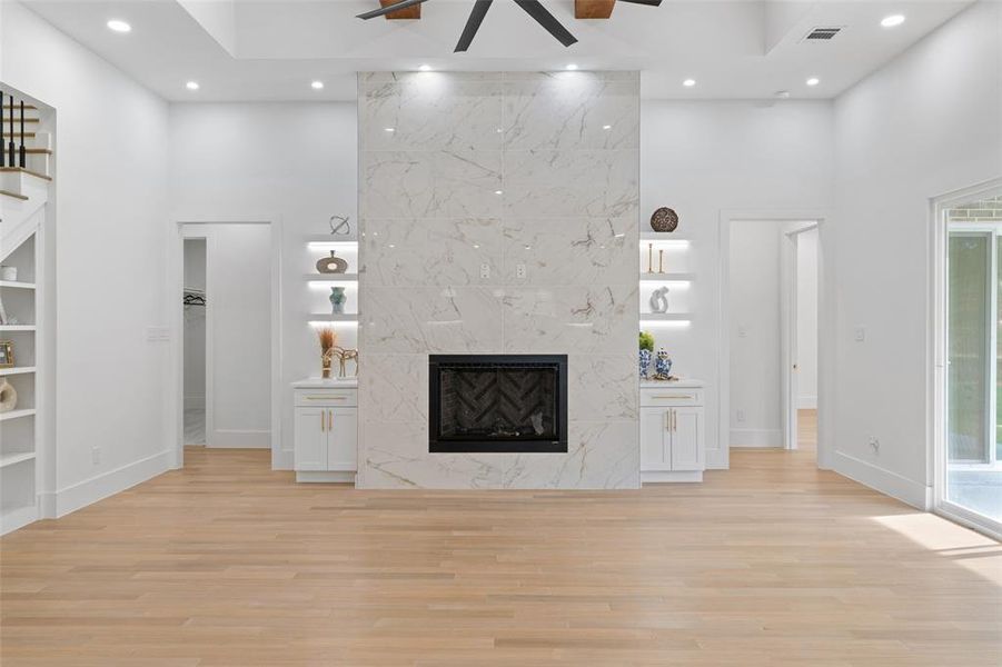 Unfurnished living room featuring a towering ceiling, a premium fireplace, recessed lighting, light wood finished floors, and built in features