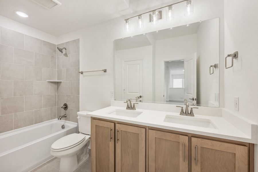 Bathroom with double sink vanity, wood cabinets, white countertop, tiled tub-shower combo, and large mirror with vanity lights