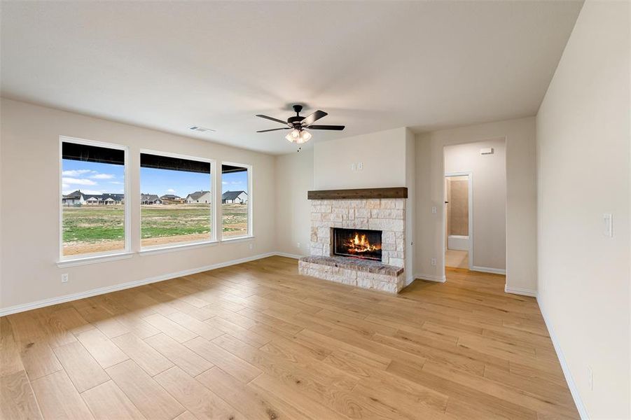 Unfurnished living room with light wood-style floors, a stone fireplace, and ceiling fan