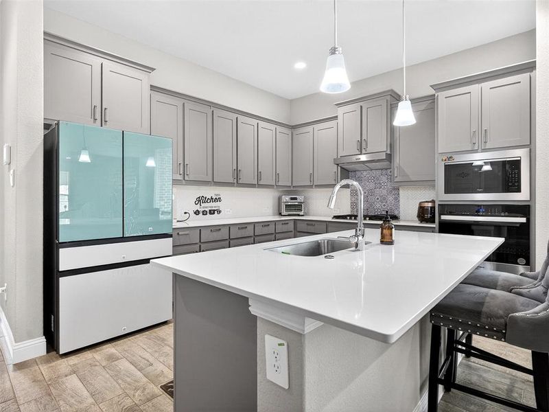 Contemporary kitchen featuring light gray cabinetry, stainless steel appliances, a white solid surface island, and wood-finish flooring Contemporary kitchen featuring light gray cabinetry, stainless steel appliances, a white solid surface island, and wood-finish flooring