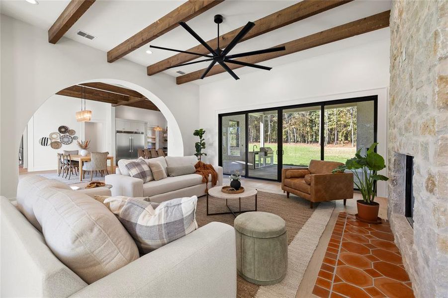Living area featuring beam ceiling, arched walkways, tile patterned flooring, ceiling fan, and a fireplace