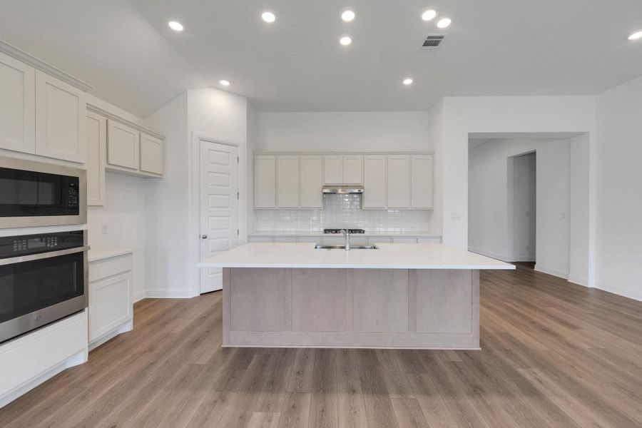 Kitchen with stainless steel oven, light countertops, a center island with sink, built in microwave, and recessed lighting