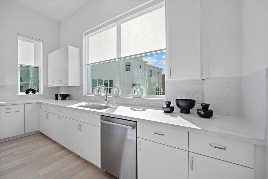 Bright kitchen featuring white cabinetry, light countertops, a stainless steel dishwasher, and wood-finish flooring