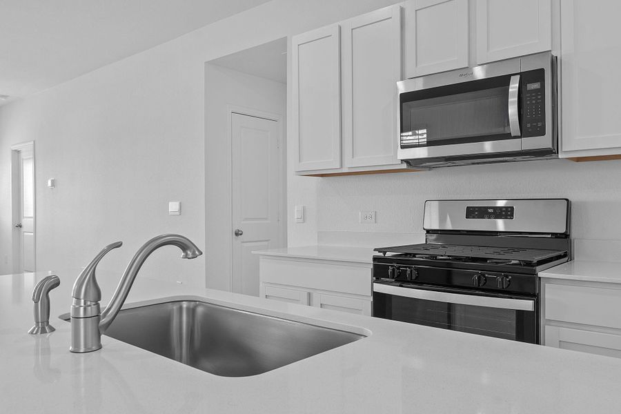 Kitchen with stainless steel appliances, white cabinets, and light stone counters