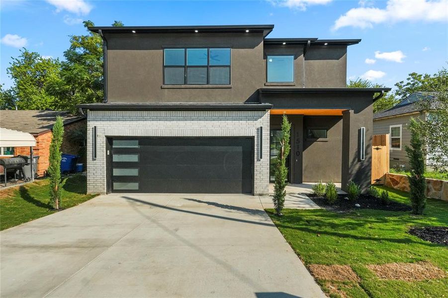Contemporary house with brick siding, stucco siding, a garage, and driveway