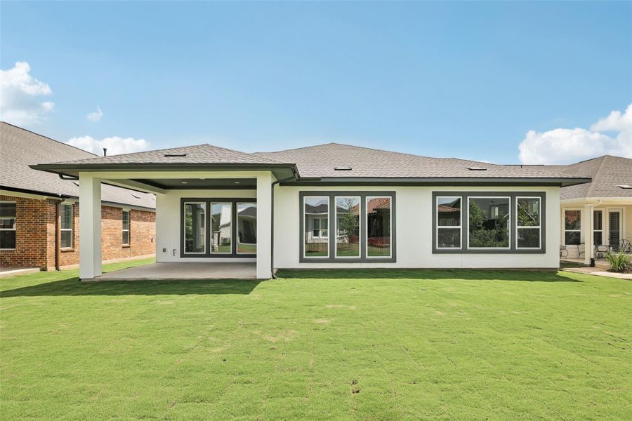 Back of property featuring stucco siding, a patio, a lawn, and a shingled roof