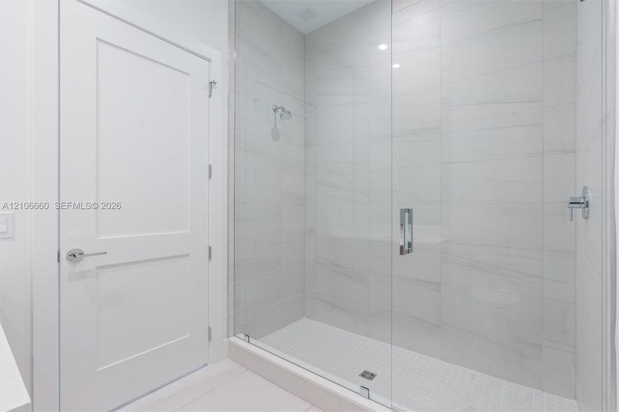 Walk-in shower featuring large-format porcelain tile surround, frameless glass enclosure, polished chrome fixtures, and built-in tiled bench