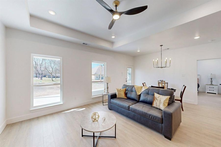 Living room with a tray ceiling, light hardwood / wood-style floors, and ceiling fan with notable chandelier