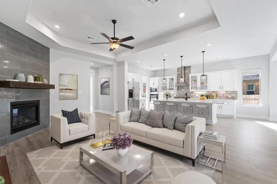 Living area featuring a tray ceiling, a tiled fireplace, light wood-style flooring, ceiling fan, and recessed lighting
