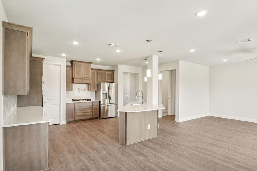 Open kitchen with tan wood cabinets, center island, stainless refrigerator, and light hardwood floors