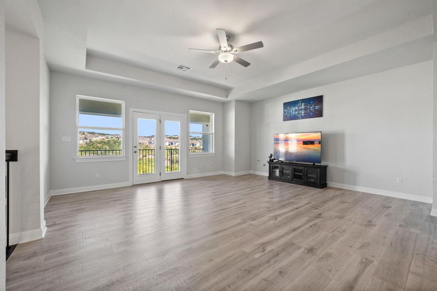 Unfurnished living room featuring a ceiling fan, a raised ceiling, and light wood-style floors