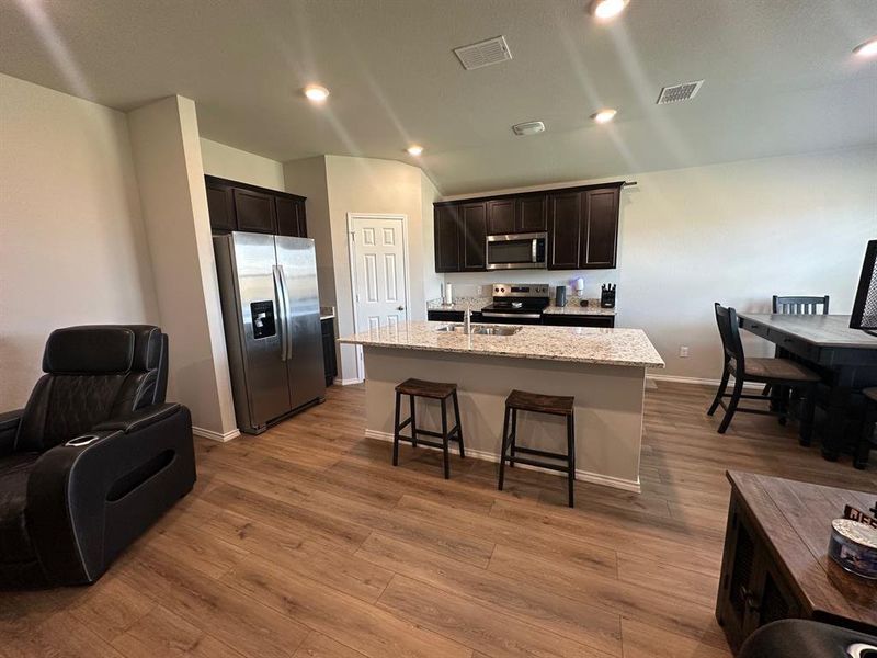 Kitchen with stainless steel appliances, light stone countertops, recessed lighting, a kitchen breakfast bar, and dark wood-style flooring