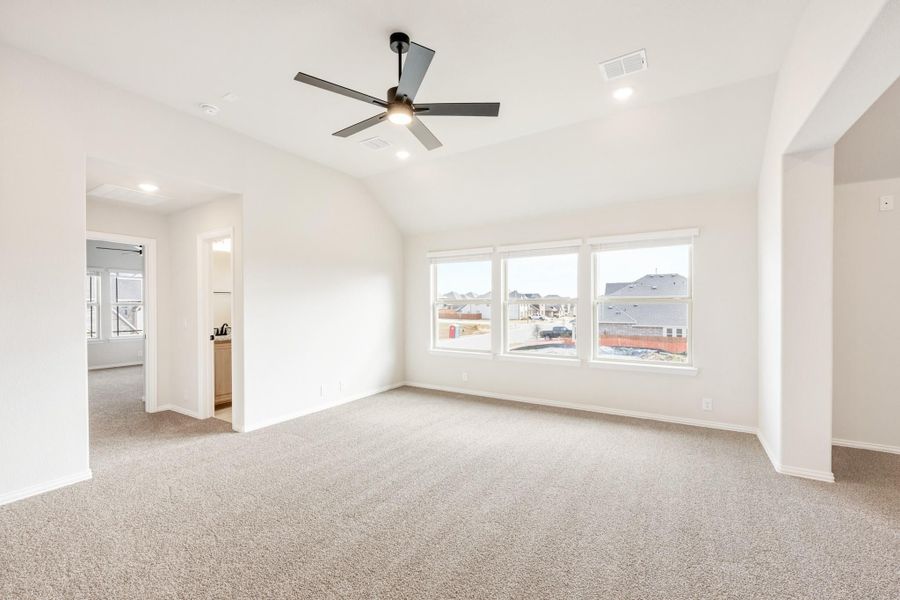 Empty bedroom with vaulted ceiling, ceiling fan, carpet flooring, and triple windows overlooking a neighborhood Empty bedroom with vaulted ceiling, ceiling fan, carpet flooring, and triple windows overlooking a neighborhood