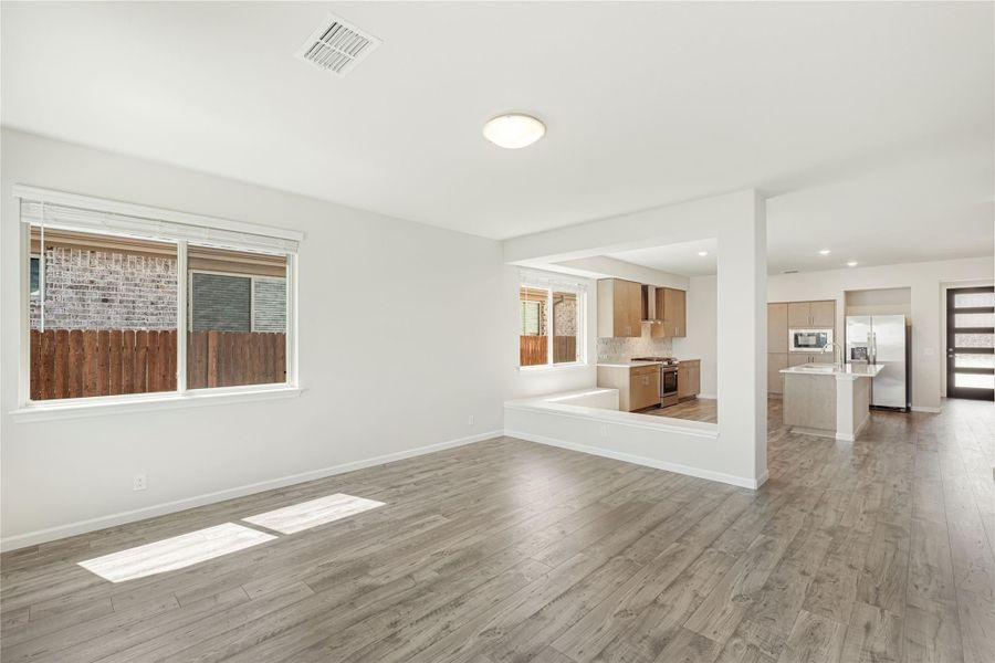 Open living area with wood floors leading to kitchen with wood cabinets and stainless steel appliances