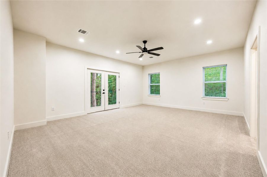 Spacious and bright Primary bedroom featuring plush carpeting, recessed lighting, and a ceiling fan, with double doors opening to lush green views.